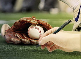 Una mazza da baseball con un guantone, una pallina e una mano con una penna