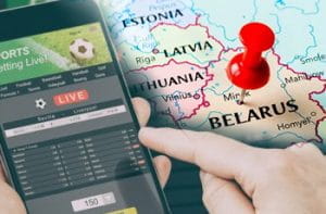 Uno smartphone connesso su un sito scommesse online, una mano che sta per premere sul display, la mappa della Bielorussia sullo sfondo