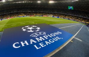 Uno stadio con le squadre che si scaldano prima dell'inizio di una partita di Champions League, con il logo della manifestazione in primo piano