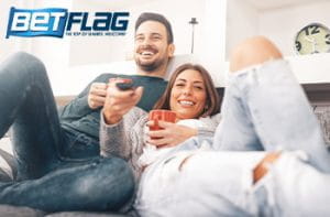Una ragazza e un ragazzo su un divano mentre guardano la tv e il logo di BetFlag