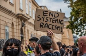Una manifestazione antirazzista e un cartello con la scritta "Stop al razzismo sistemico" in inglese