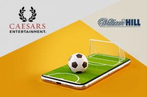 I loghi di Caesars Entertainment e William Hill e un campo di calcio stilizzato sullo schermo di uno smartphone