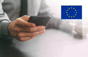 Una persona tiene in mano uno smartphone, logo dell’Unione Europea
