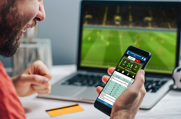 Scommettitore impegnato con app scommesse su smartphone e laptop